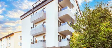 A multi-story residential building with balconies, a garage, and a staircase leading to the entrance.