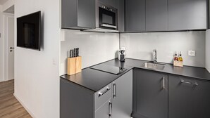 Una cocina moderna con armarios grises, horno empotrado, un lavabo y un bloque para cuchillos.