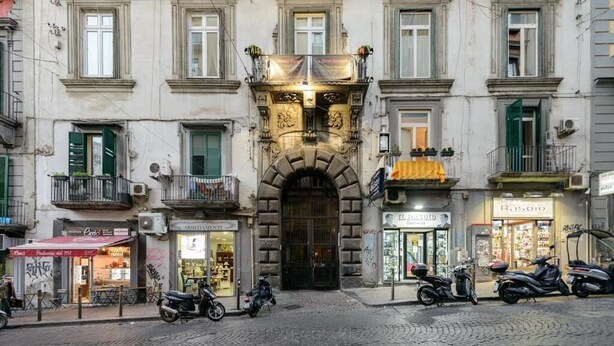 A historic building with a central entrance, shops on the ground floor, and parked scooters on the street. - Dimorart Sant'Anna (Naples)