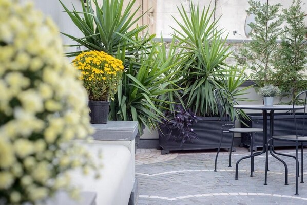 Un espace extérieur aménagé en patio, avec des plantes en pot, un coin salon et un sol carrelé.