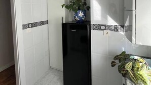 A compact kitchen with white walls, a black refrigerator, a clock, and a potted plant.