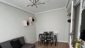 A modern living room with a grey sectional sofa, a glass coffee table, a dining area with a white table and dark chairs, and a ceiling light fixture.