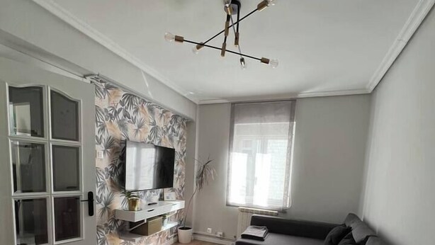 A modern living room with a glass dining table, a sofa, and a TV mounted on the wall.