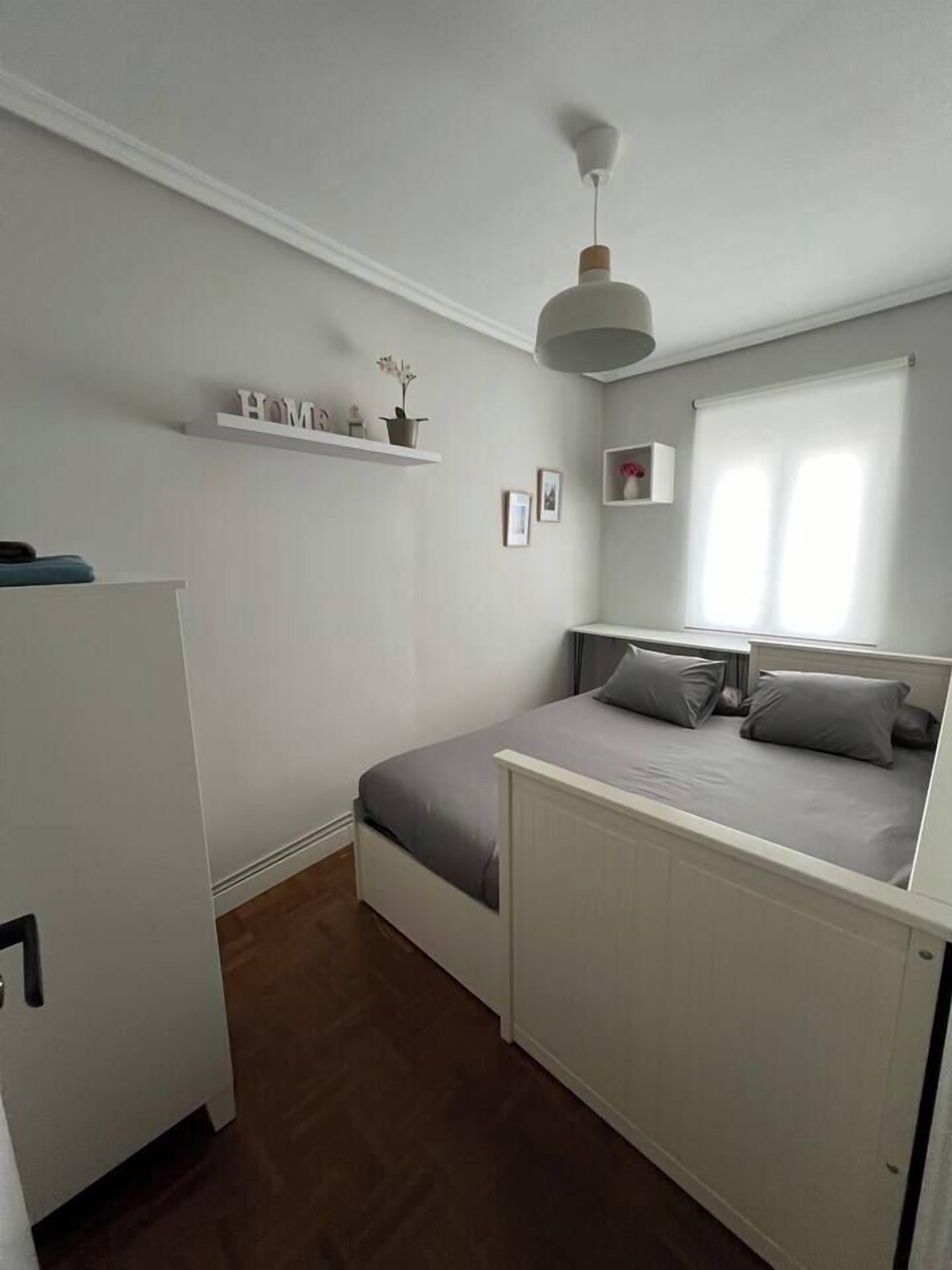 Une chambre à coucher de taille réduite, comprenant un lit, un petit bureau et une fenêtre avec des stores.