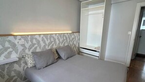 A bedroom with a bed, a headboard with a light fixture, a patterned wallpaper, and a wooden floor.