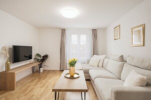 Una sala de estar moderna con televisor de pantalla plana, mesa de centro de madera, sofá color beige y un amplio ventanal con cortinas.
