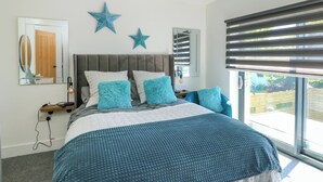 A bedroom with a large bed, a grey headboard, and two star decorations on the wall. - Iscoed (Rhosneigr)