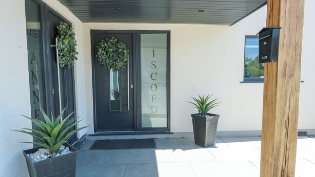 A modern building entrance with a dark door, a welcome mat, and two potted plants. - Iscoed (Rhosneigr)