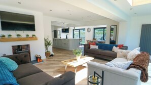 A spacious living area with a sofa, a coffee table, and a TV mounted on the wall. - Iscoed (Rhosneigr)