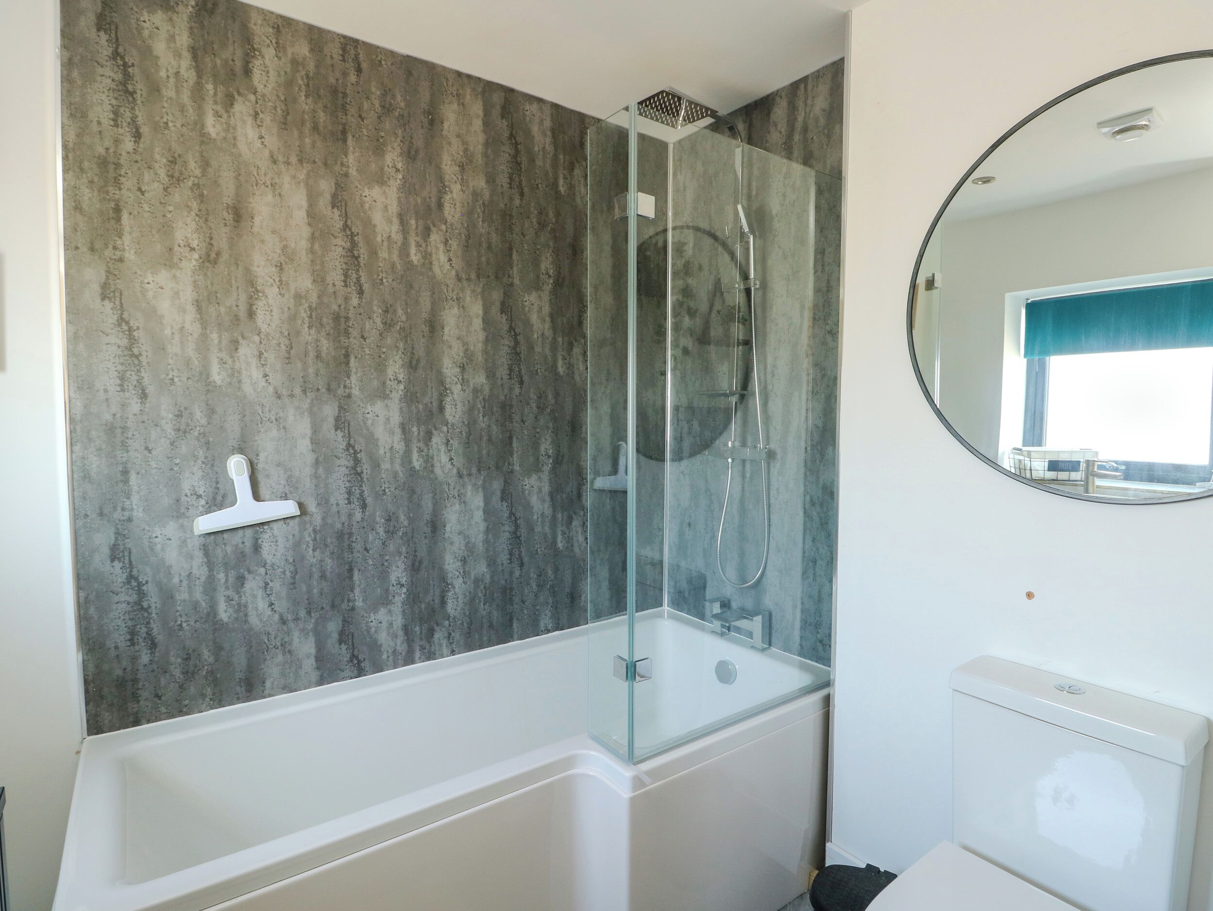 A modern bathroom with a glass-enclosed shower, a white bathtub, and a round mirror.