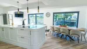 A modern kitchen with a large island, pendant lighting, and a dining area with a view of the outdoors. - Iscoed (Rhosneigr)