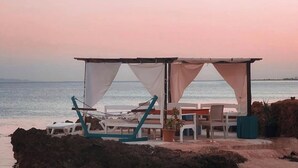 Un cabanon de plage avec une table et des chaises, un hamac et une vue sur la mer.