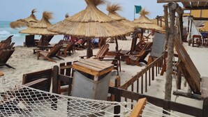 Une plage avec des chaises longues en bois et des parasols en chaume.