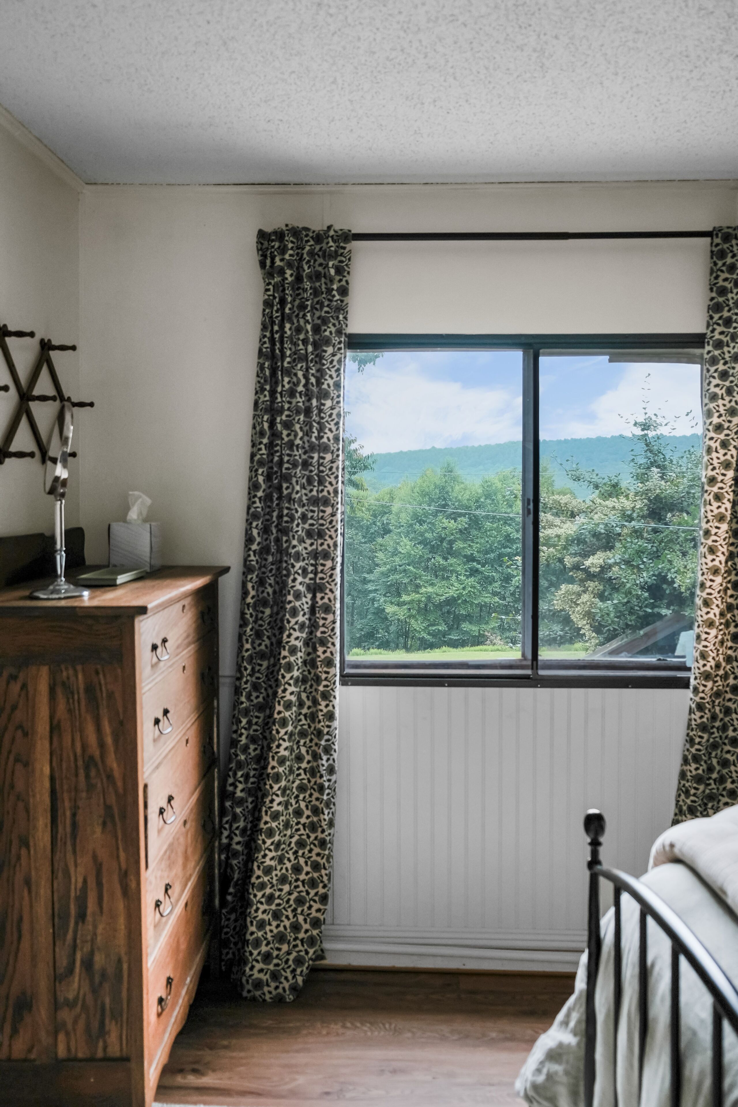 Een slaapkamer met een groot raam, een houten dressoir en een bed.