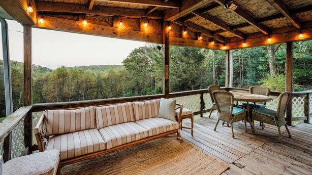 A wooden deck with a sofa and chairs, a table, and a view of a forested area.