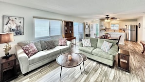 A spacious living room with a sectional sofa, a coffee table, and a dining area with a kitchen in the background. - Polo Garden Villa - 1/1 Villa On the Polo Field w/ Amazing Garden in The Village of Santiago (Santiago, The Villages)