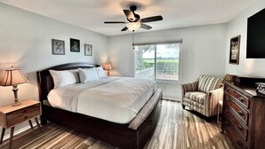 A bedroom with a bed, a ceiling fan, a nightstand, a dresser, and a window with a view of the outdoors. - Polo Garden Villa - 1/1 Villa On the Polo Field w/ Amazing Garden in The Village of Santiago (Santiago, The Villages)