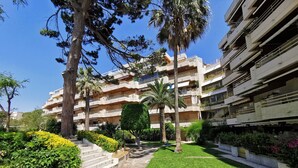 A multi-story residential building with balconies, a well-maintained lawn, and various trees. - BEACH FRONT APARTMENT (Salou)