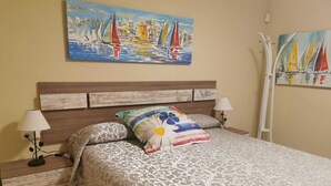 A neatly made bed with patterned bedding, a wooden headboard, and two bedside lamps. - BEACH FRONT APARTMENT (Salou)