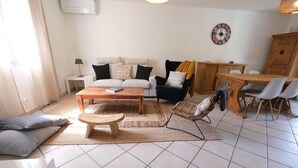 Un salon comprenant un canapé, une table basse, une table à manger avec des chaises, une lampe et une horloge murale.