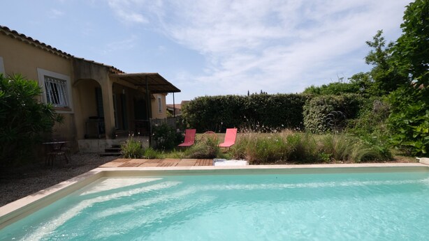 Une piscine à l’eau d’un bleu limpide, entourée d’un jardin où poussent différentes espèces de plantes, et une terrasse aménagée avec des chaises.