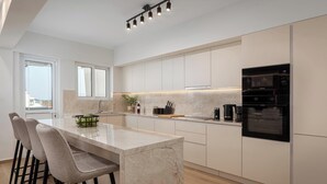 Una cocina moderna con una isla de mármol, taburetes de bar, electrodomésticos integrados y ventanas amplias.
