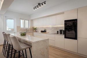 Una cocina moderna con una isla de mármol, taburetes de bar, electrodomésticos integrados y ventanas amplias.