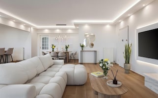 Una sala de estar moderna con un sofá modular, un comedor con mesa y sillas, y un televisor de pantalla plana montado en la pared.