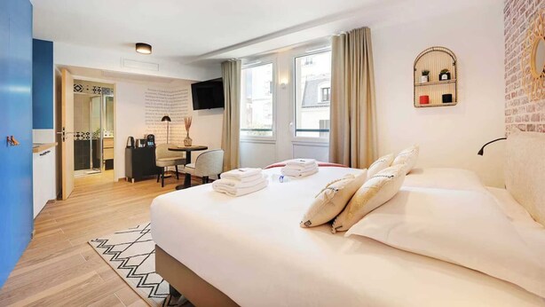Habitación de hotel con una cama grande, un escritorio, una silla y un televisor en la pared.