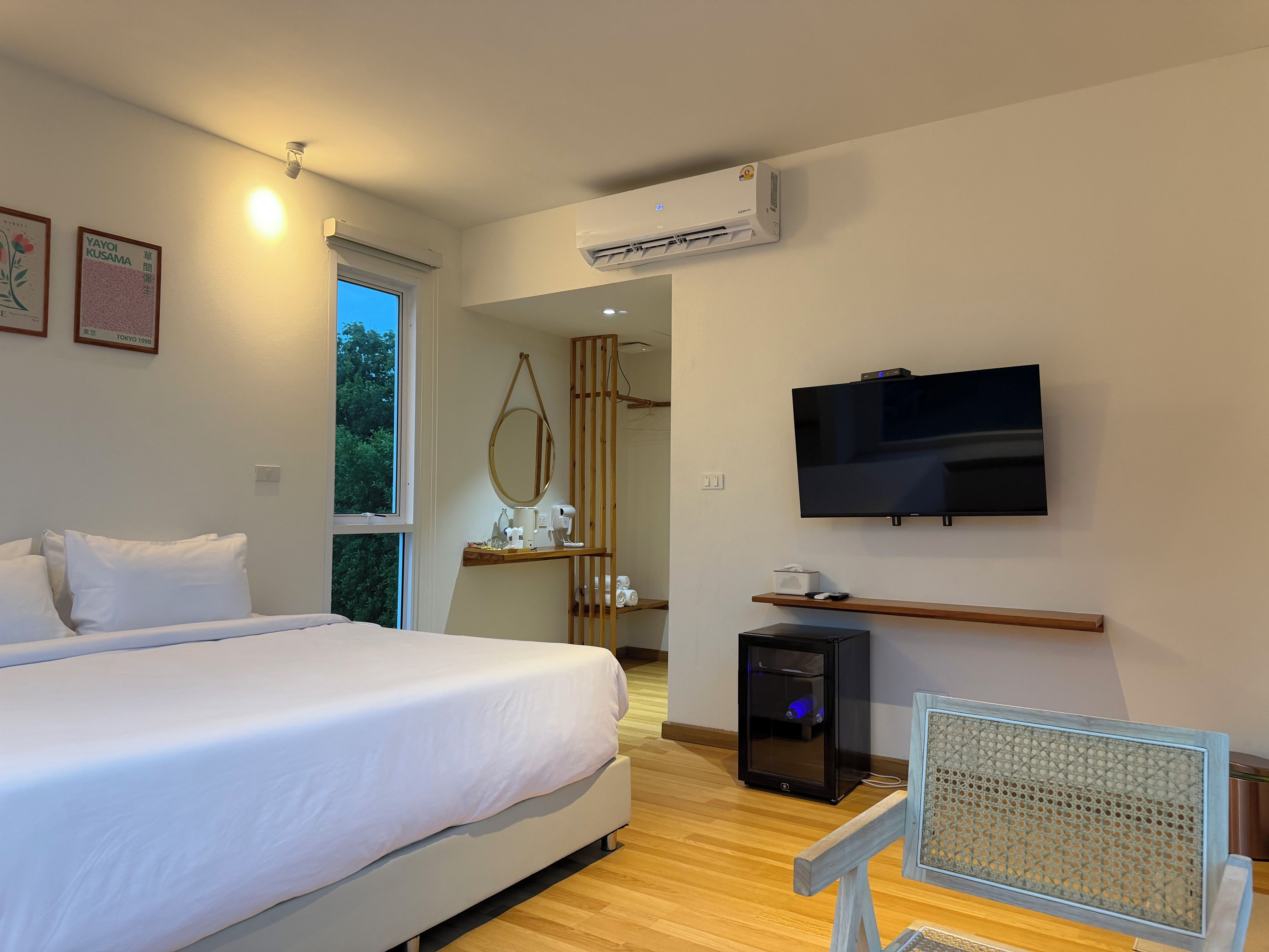 Una camera d'albergo con un letto, televisione, condizionatore d'aria, una scrivania con un computer e una finestra.