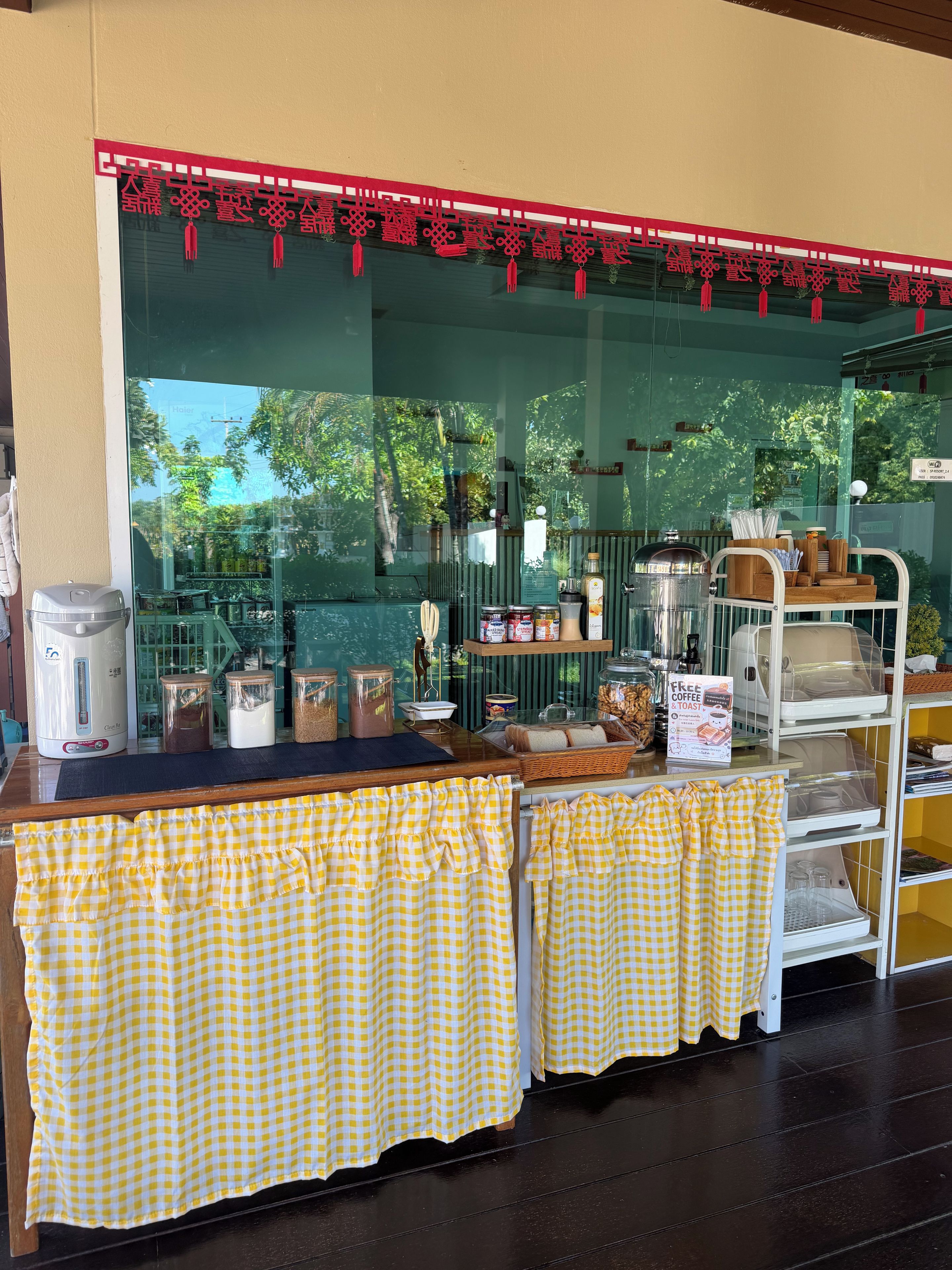 A cafe with a counter, checkered tablecloths, and various food items displayed.