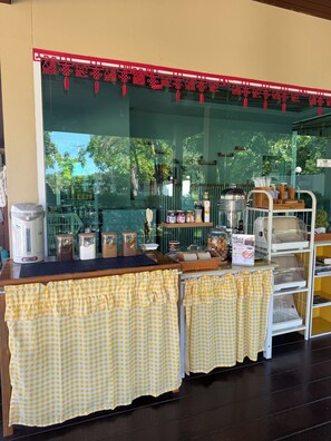 A cafe with a counter, checkered tablecloths, and various food items displayed. - SP RESORT (Wichian Buri)