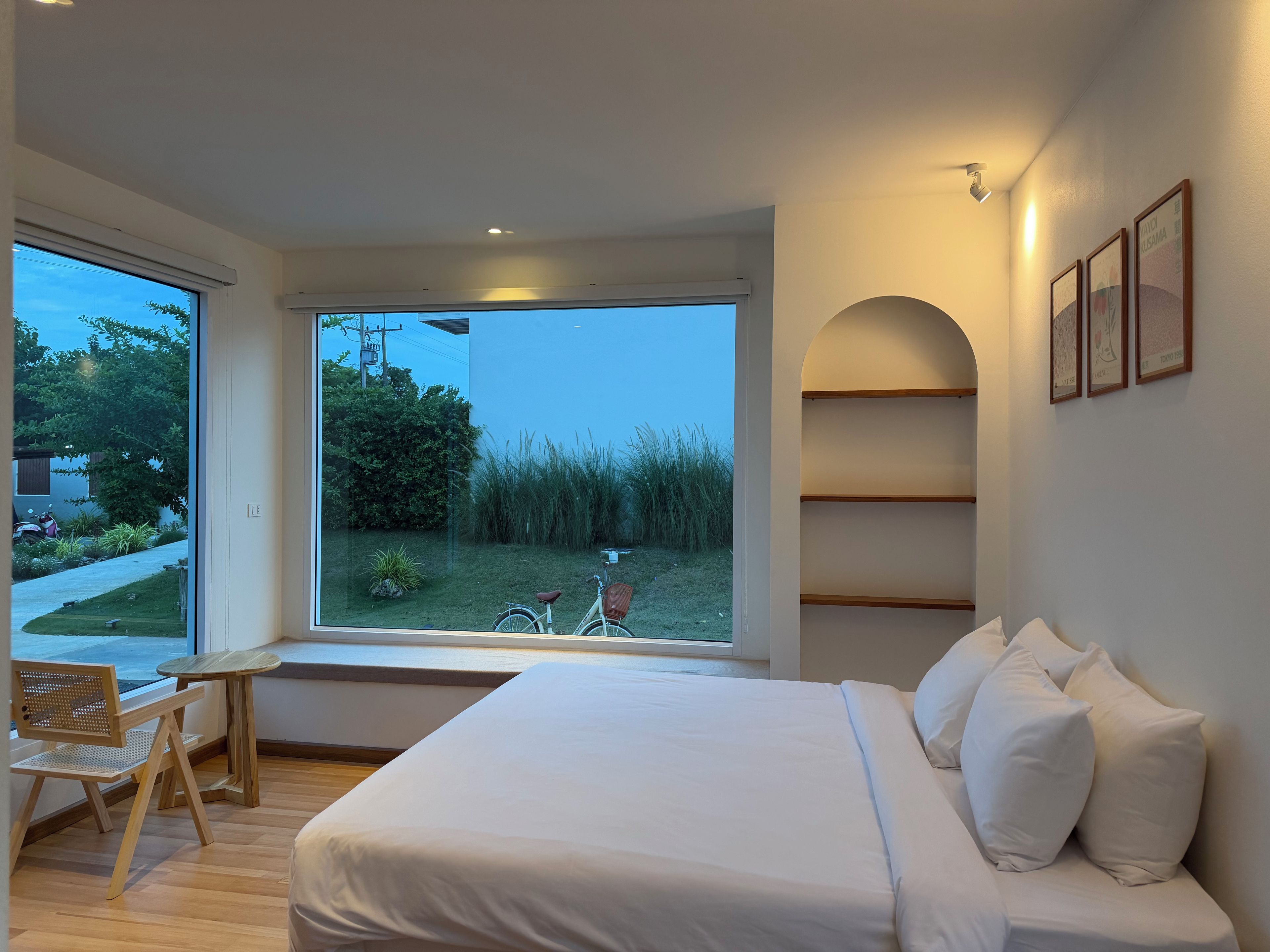 Un dormitorio con un ventanal grande, una cama, una silla y una mesita.