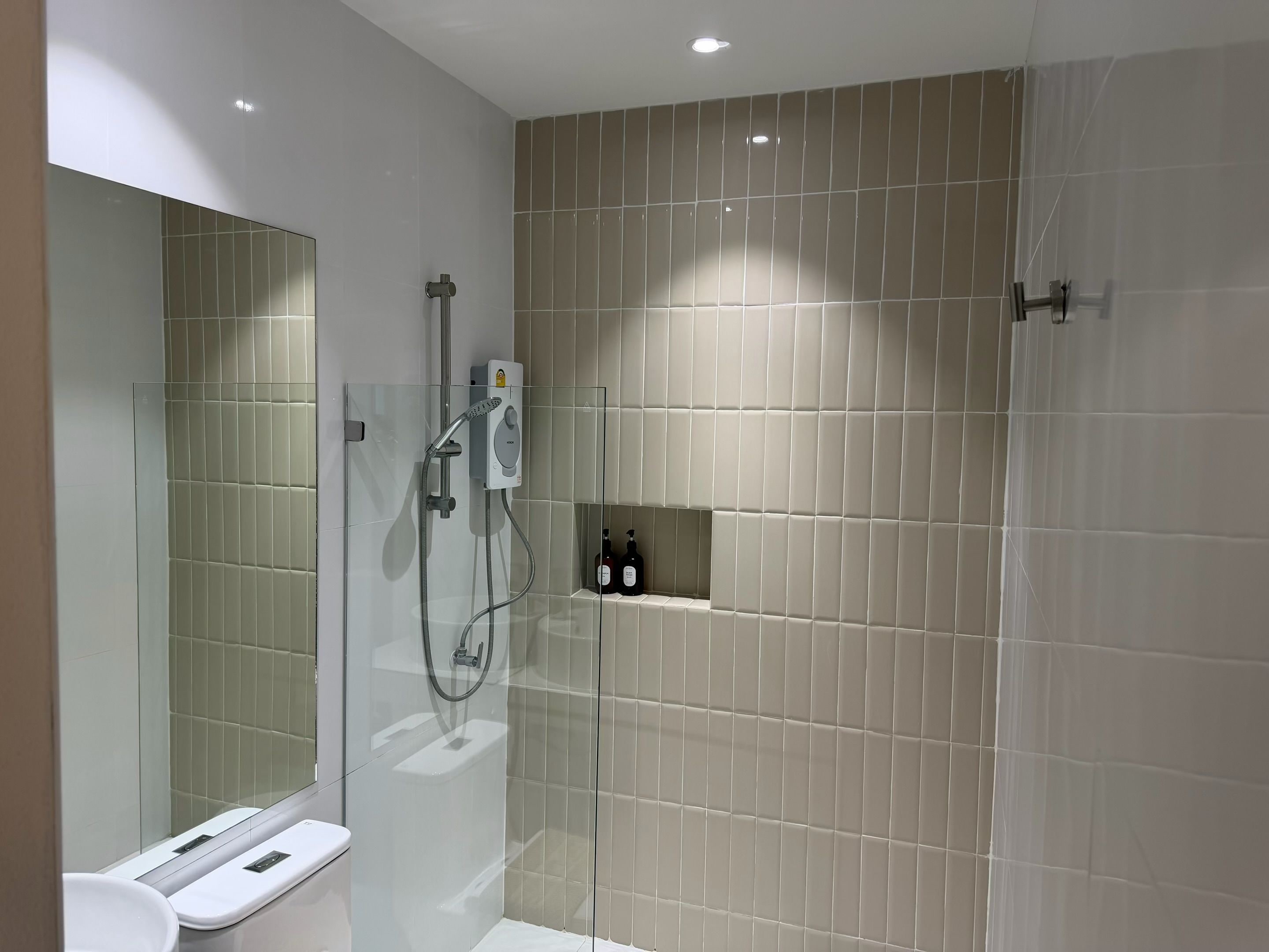 A modern bathroom with a glass-enclosed shower, a toilet, and a shelf with toiletries.