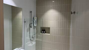 A modern bathroom with a glass-enclosed shower, a toilet, and a shelf with toiletries.