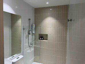 A modern bathroom with a glass-enclosed shower, a toilet, and a shelf with toiletries. - SP RESORT (Wichian Buri)