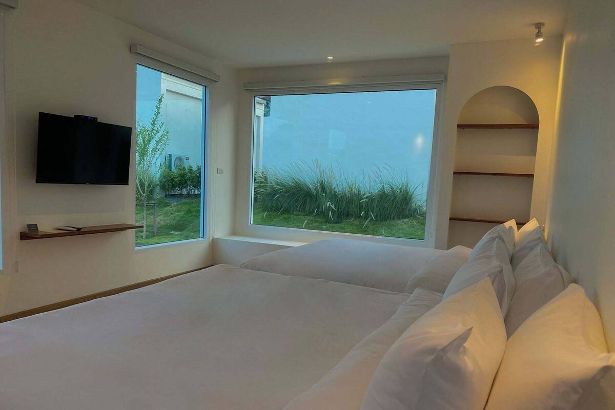 A modern bedroom with a large bed, a TV mounted on the wall, and a view of the outdoors.