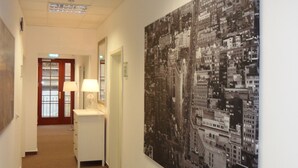 A hallway with a large cityscape painting on the wall, a desk with a lamp, and a door at the end. - Economy Hotels Kronach (Kronach)