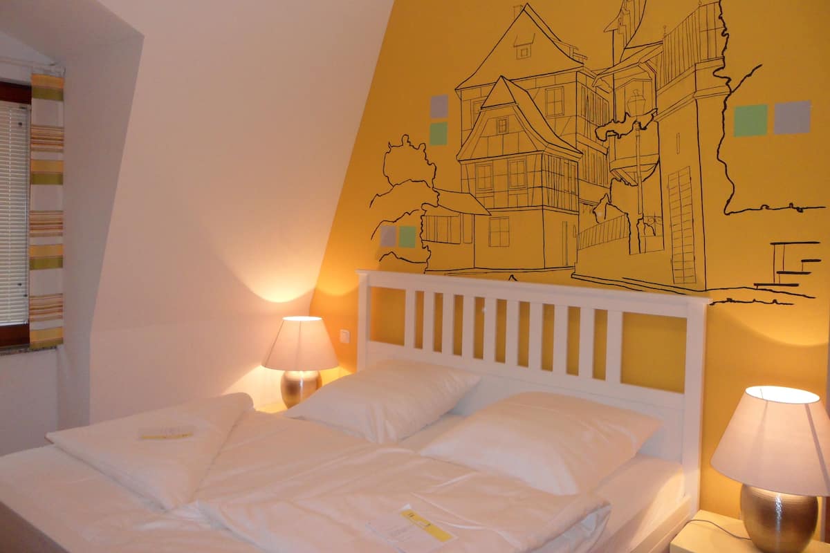 A hotel room with a bed, two bedside lamps, and a wall mural of a building.
