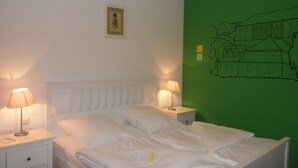 A neatly made bed with white linens, two bedside lamps, a small bedside table, and a green wall with a simple line drawing. - Economy Hotels Kronach (Kronach)