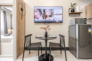 A modern kitchen with a dining area, a flat-screen TV mounted on the wall, and a refrigerator.
