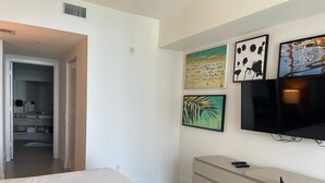 A bedroom with a bed, a dresser, a TV, and artwork on the wall.