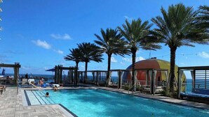 A pool area with a wooden deck, lounge chairs, and palm trees. - Wonderful Views at Lyfe Resort @rent4us (Hollywood)