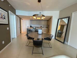 A modern kitchen with a central island, a dining area with a round table and chairs, and a large mirror on the wall.