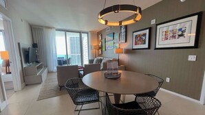 A modern living room with a round dining table, black wicker chairs, a sofa, and a TV.