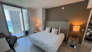 A modern hotel room with a large bed, two bedside tables with lamps, a chair, and a view of a cityscape through a large window. - Wonderful Views at Lyfe Resort @rent4us (Hollywood)
