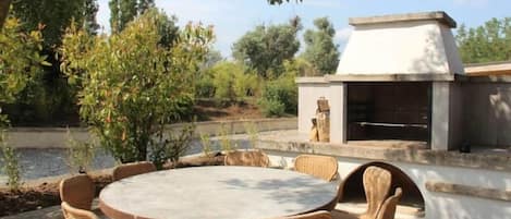 An outdoor dining area with wicker chairs and a round table, a barbecue grill, and a view of a body of water.