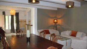 A modern dining area with a wooden table, chairs, and a glass-top coffee table. There is a sofa with cushions and a floor lamp in the background. - Casa Kathy (Pertuis)