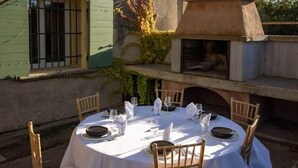 A round table set for a meal with chairs, a brick oven, and a window with bars.