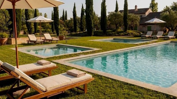 A rectangular pool with two separate sections, surrounded by well-maintained grass and trees. There are lounge chairs and umbrellas providing shade.